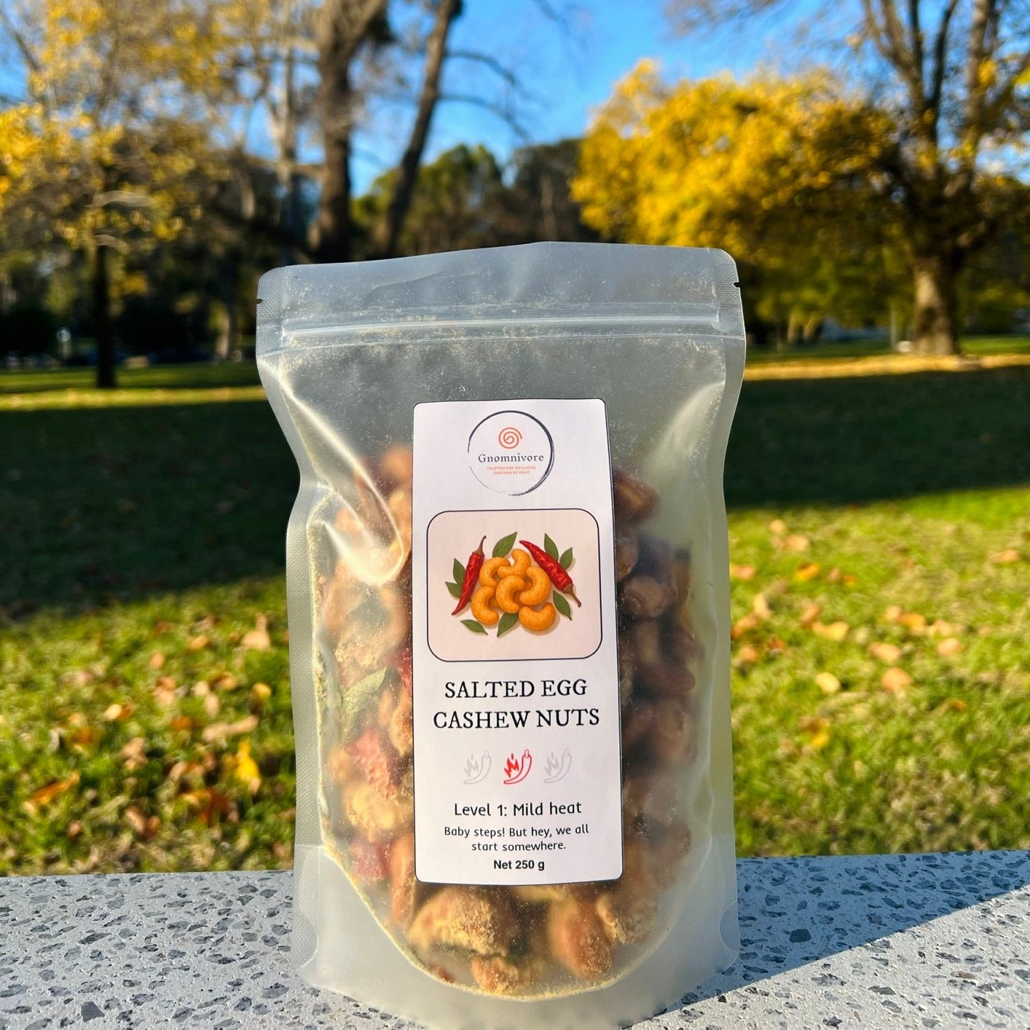 Packaged salted egg cashew nuts with a label in a park setting