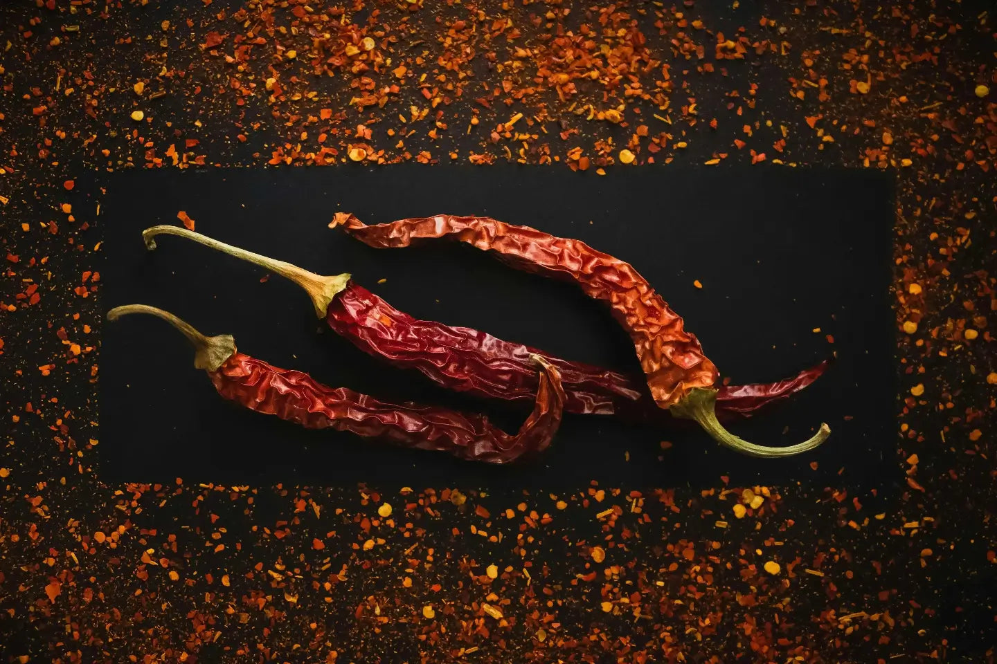 Dried red chili peppers on a dark surface with a spice background. Gnomnivore engineered spicy snacks.