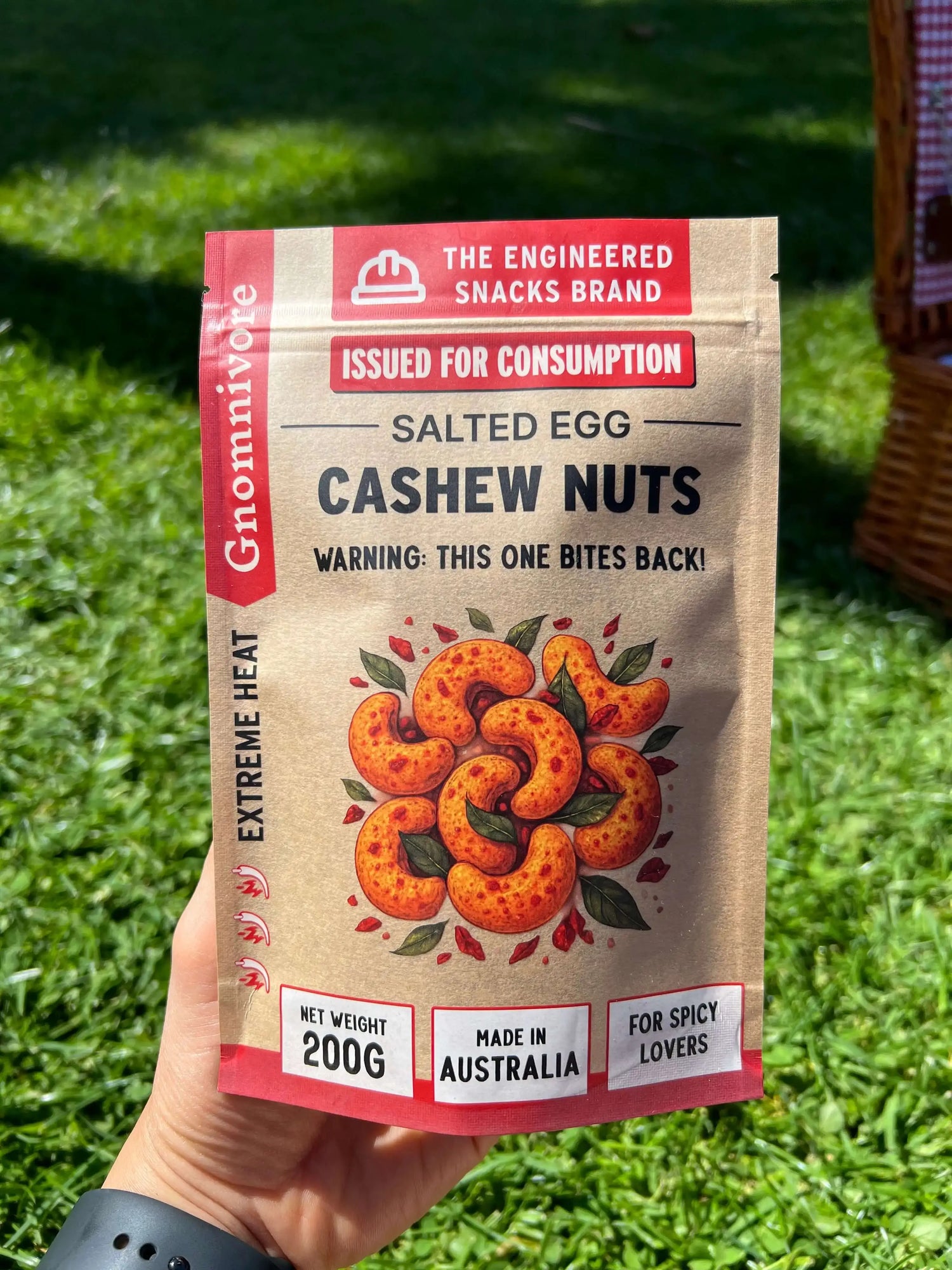 Packaged salted egg cashew nuts with branding and warning label held in front of grass. Gnomnivore engineered spicy snacks.