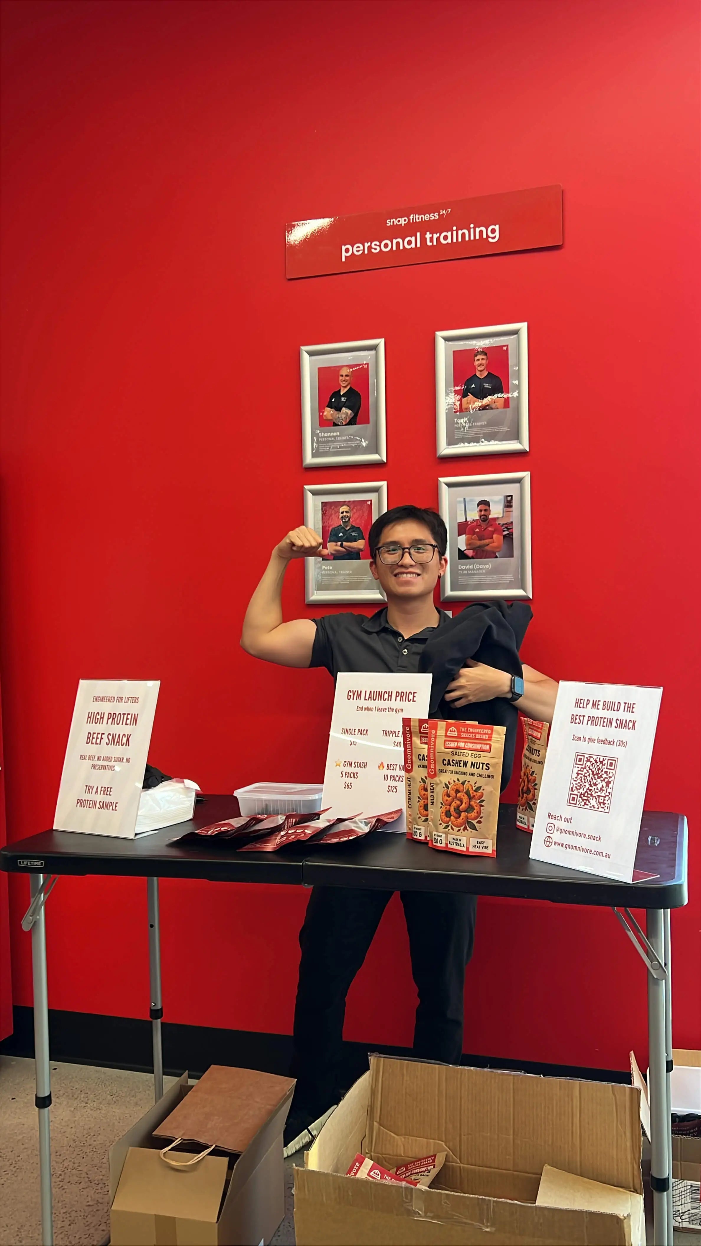 An Engineer standing at a table with promotional materials against a red wall at the gym