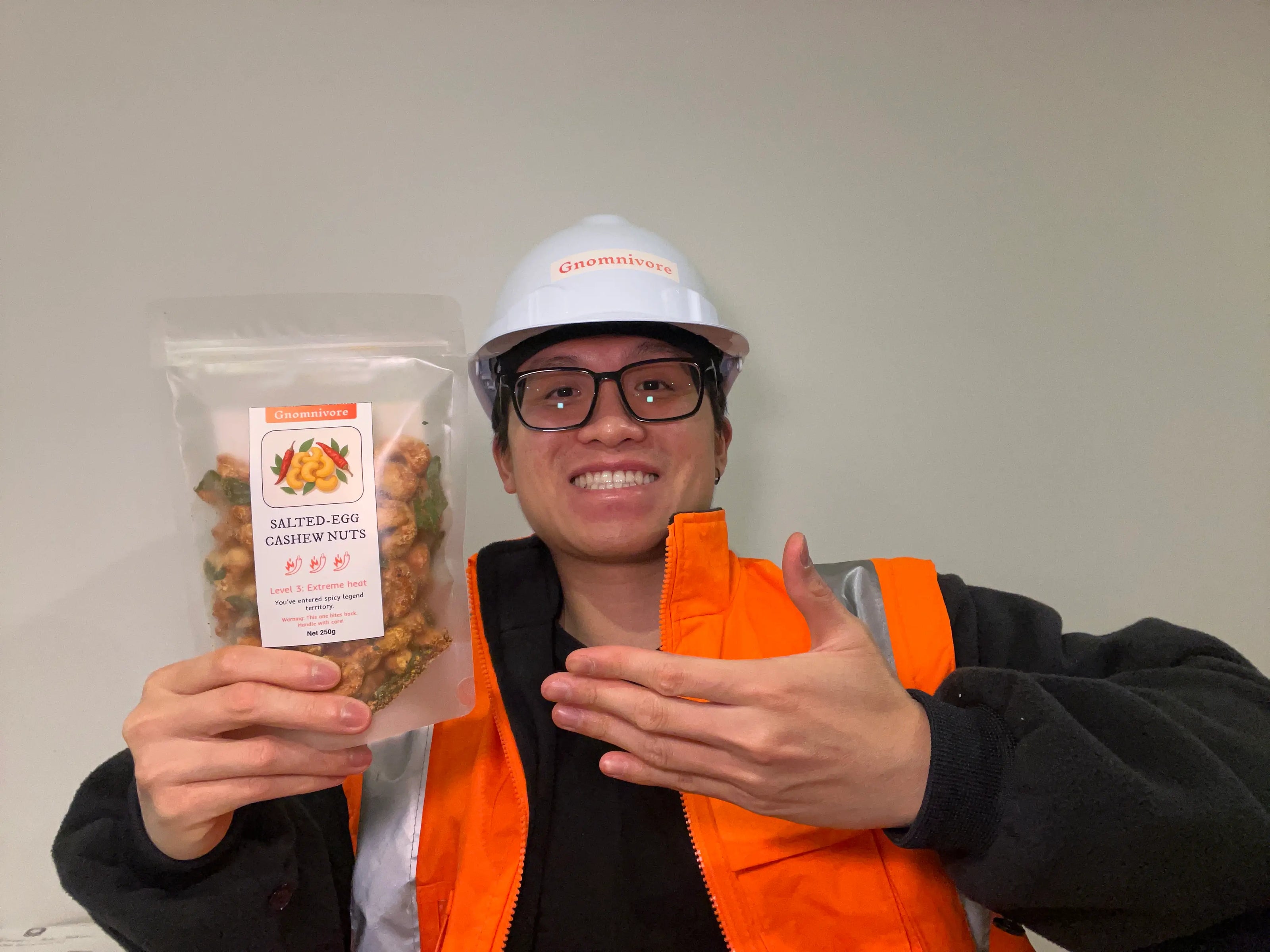 Person wearing a hard hat and safety vest holding a package of engineered spicy snacks nearby
